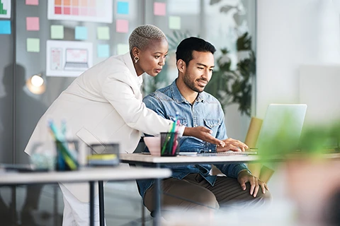 Two asset finance professionals looking at a laptop discussing ways to reduce operational expense,